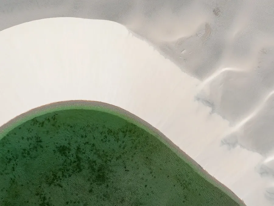 Lagoa de tom esverdeado encaixada entre dunas brancas, vista de cima