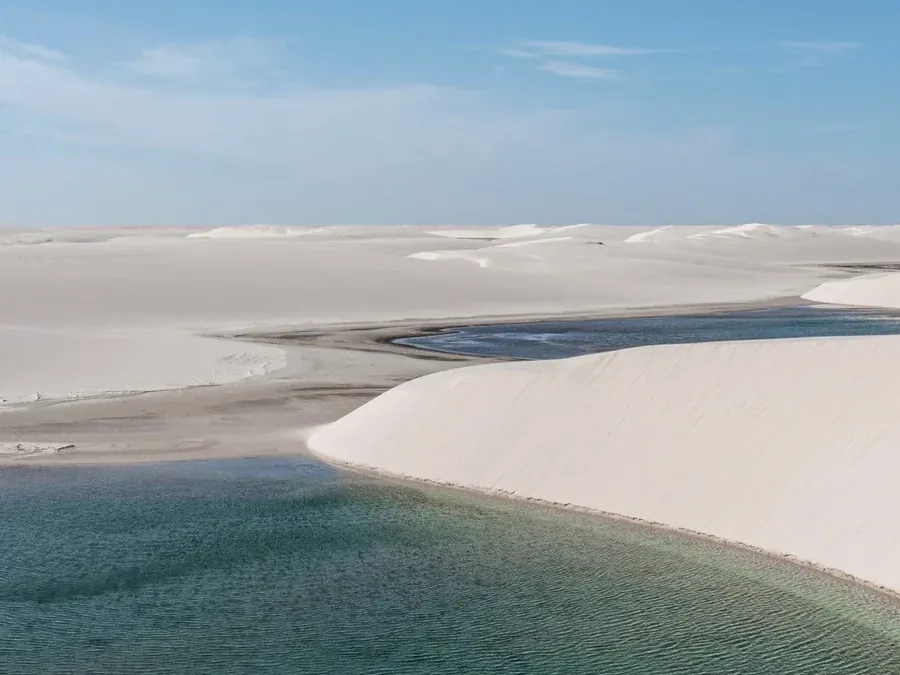 Lagoa de água clara refletindo o céu entre dunas brancas