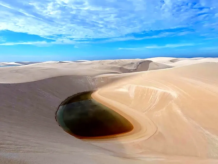 Duna branca com uma pequena lagoa escura ao pé, sob céu de manhã