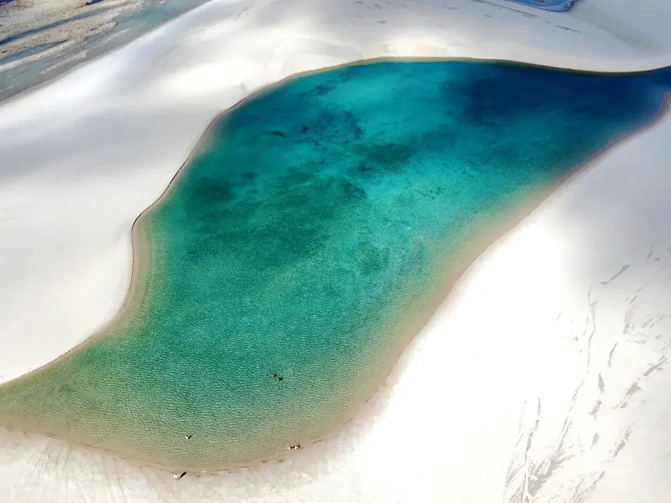 Vista aérea de uma lagoa turquesa encaixada entre dunas de areia branca