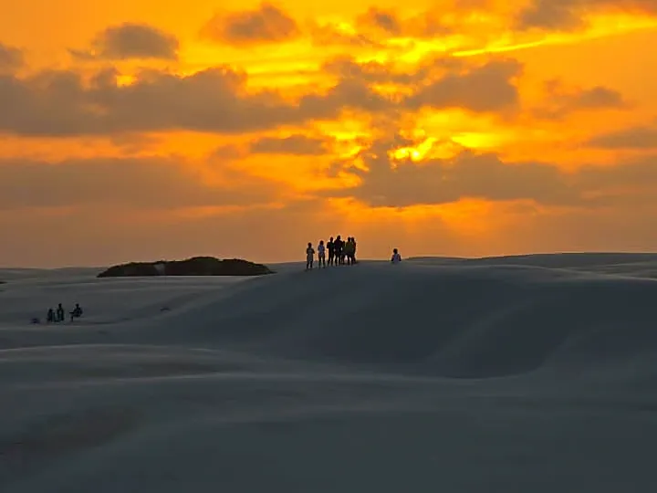 Silhuetas de pessoas no alto de uma duna durante o pôr do sol dourado nos Lençóis
