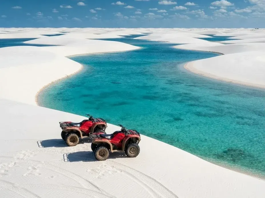 Dois quadriciclos vermelhos parados na crista de uma duna branca de Santo Amaro, com uma lagoa turquesa logo abaixo