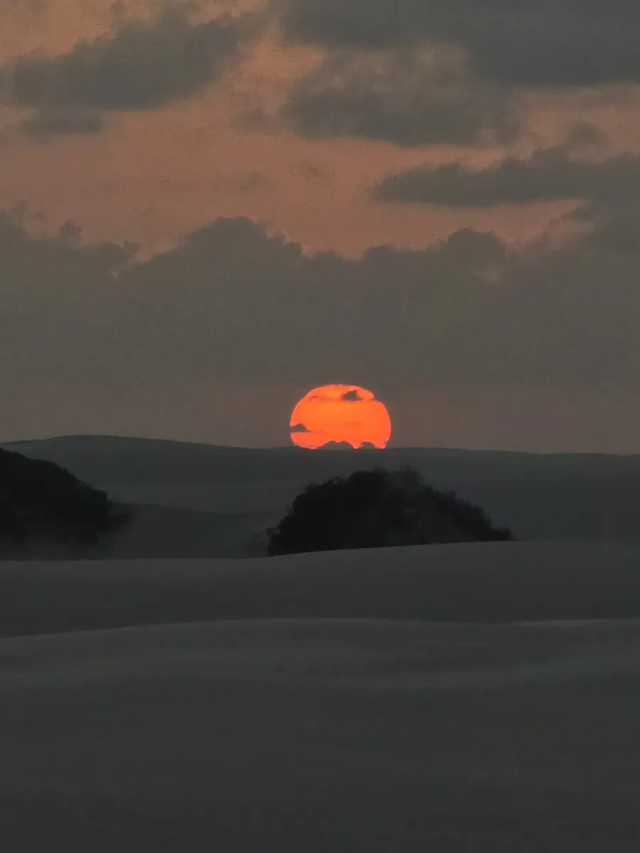 Sol alaranjado tocando a linha das dunas no fim da tarde