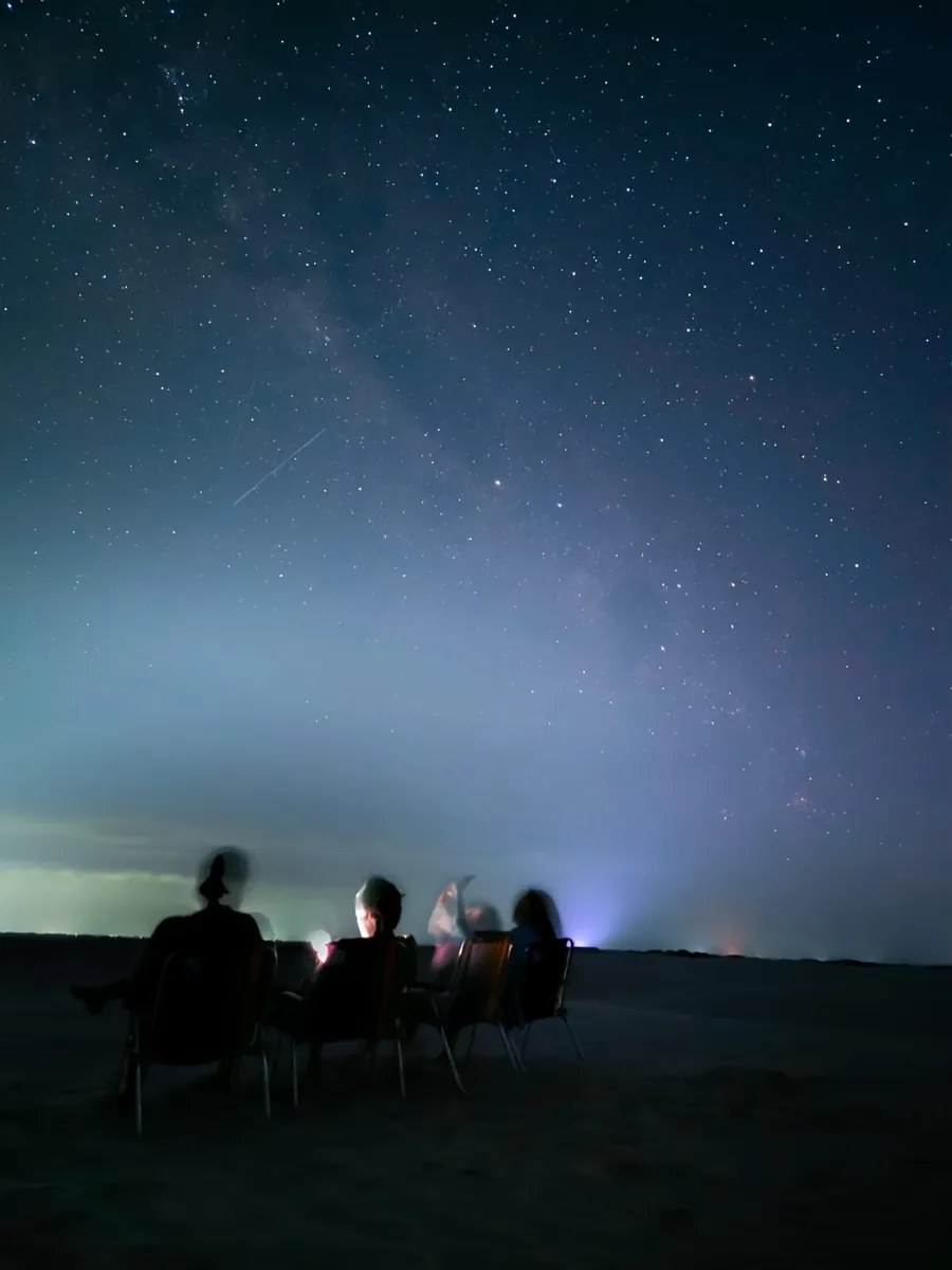 Grupo sentado nas dunas sob o céu estrelado